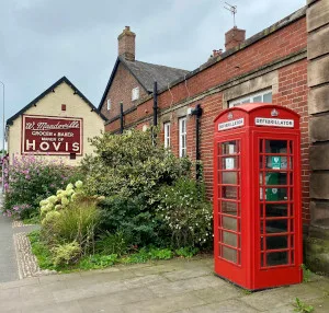 Hovis sign on the wall of Manderville's bakery in Holmes Chapel. A red telephone box, with a Defibrillator sign is to the right of the image.